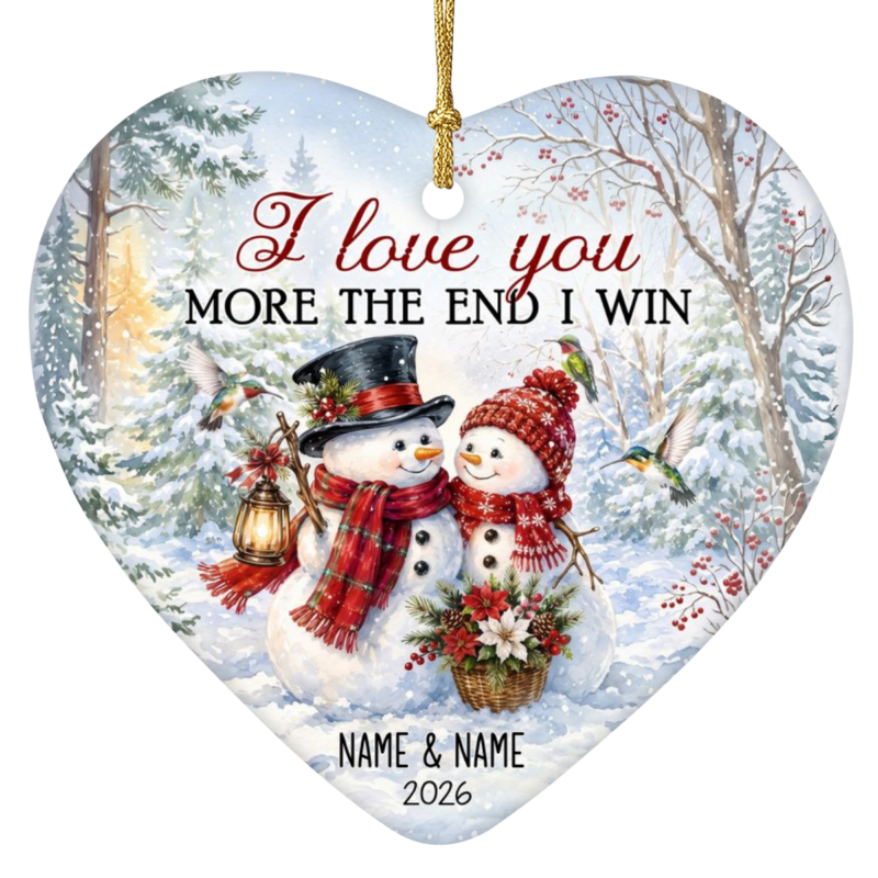 I Love You More the End I Win ornament in a heart-shaped ceramic design featuring a snowman couple bundled in scarves and hats with hummingbirds in a snowy forest, personalized with "James & Selena 2026"